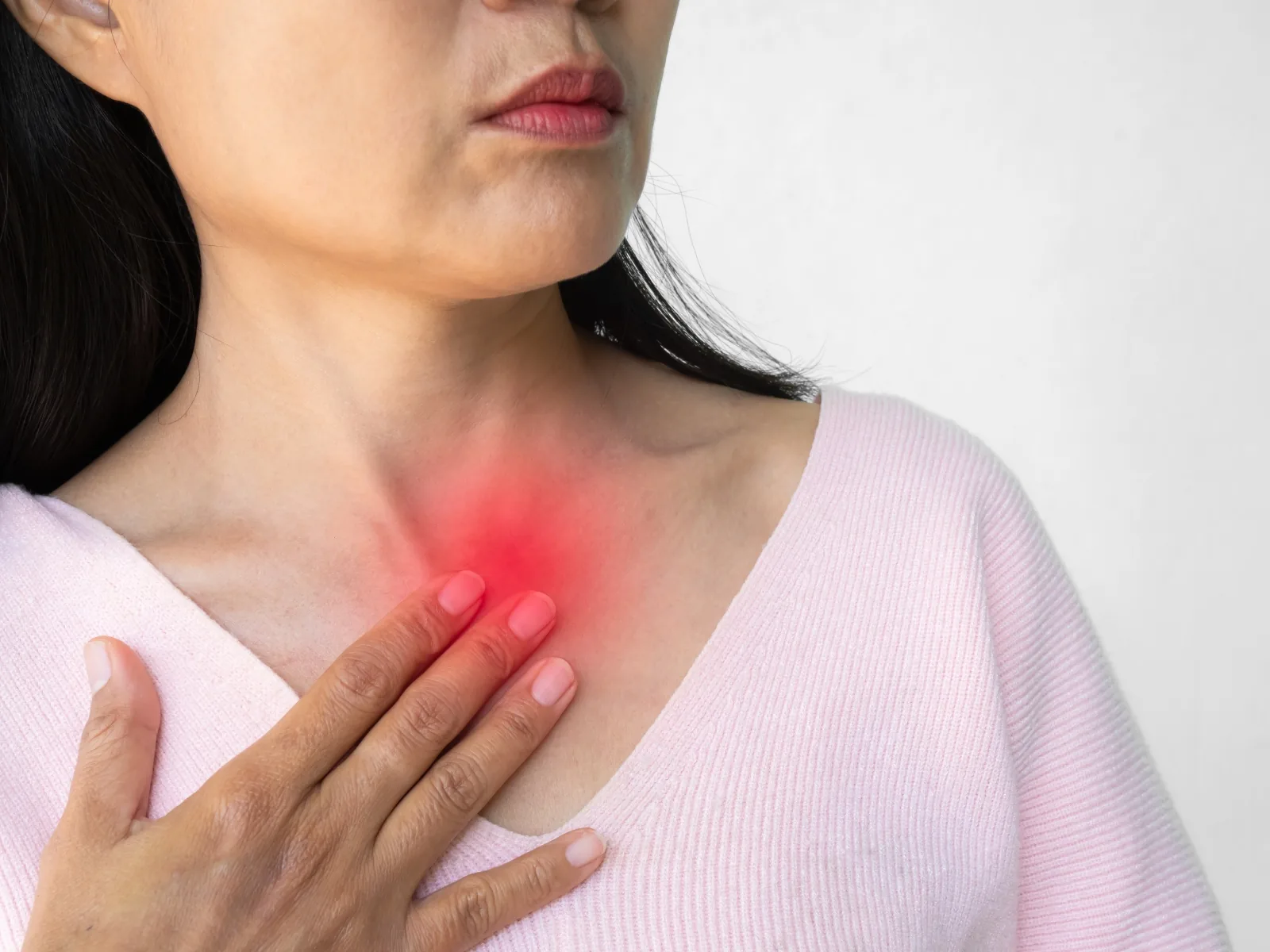 A woman resting a hand against the base of her throat, where a red glow marks the burning of acid reflux — the condition that can quietly wear away tooth enamel.